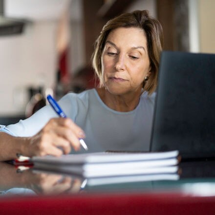 A person researching how to go back to college on a laptop and taking notes with a pen.
