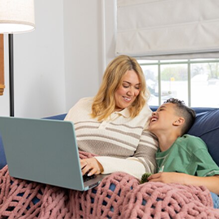SNHU graduate Madison Richards and her son Malakai sitting on a couch while she works on a laptop, completing her online degree program.