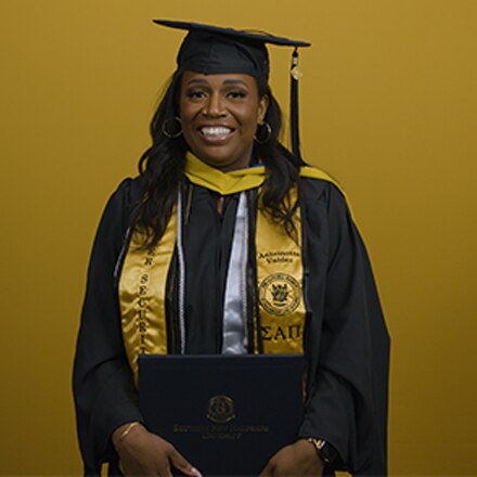 An SNHU graduate wearing an honor society stole and holding her diploma at her commencement ceremony.