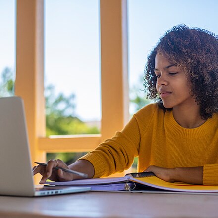  A student in a yellow sweater sitting at a desk working on her minor on her laptop