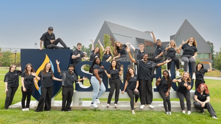 A group of students on campus in front of the SNHU logo.