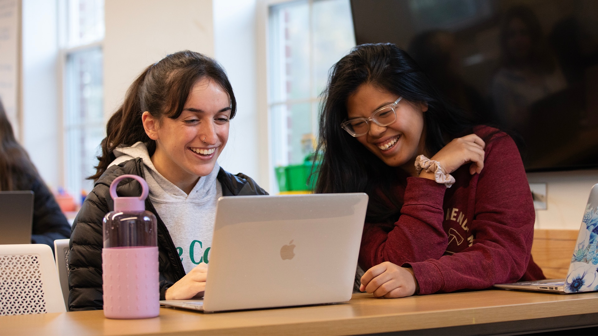 Two individuals looking into a laptop, laughing and talking.