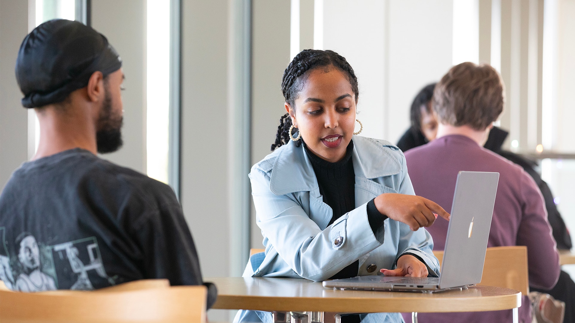 A group of two individuals sitting across a table and one of them shows the other one something on their laptop.
