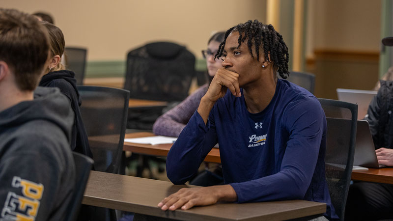 A student sitting with other students in a classroom listening attentively to a lecture.