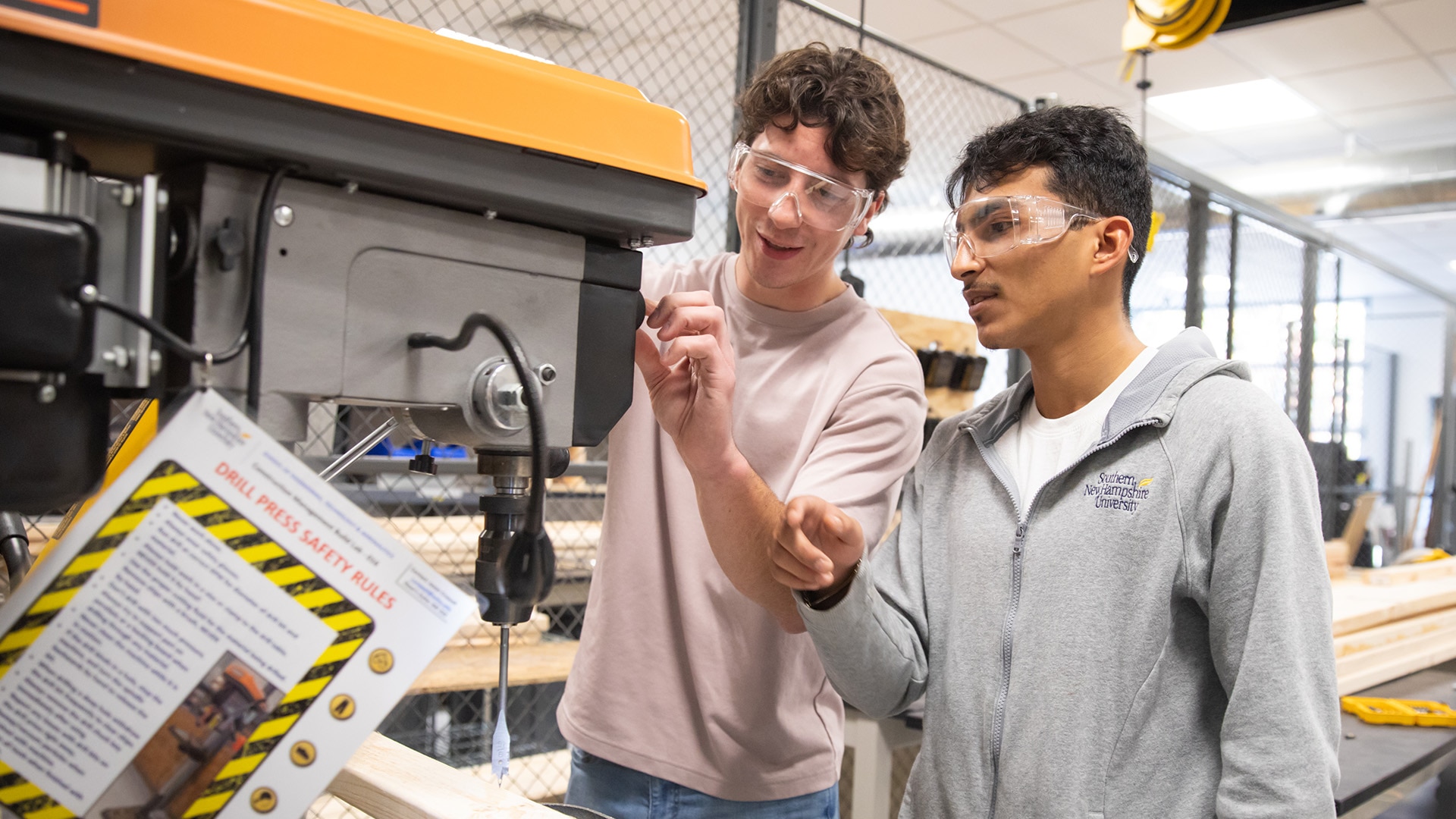 Two students talking and learning to operate the drill press machine.