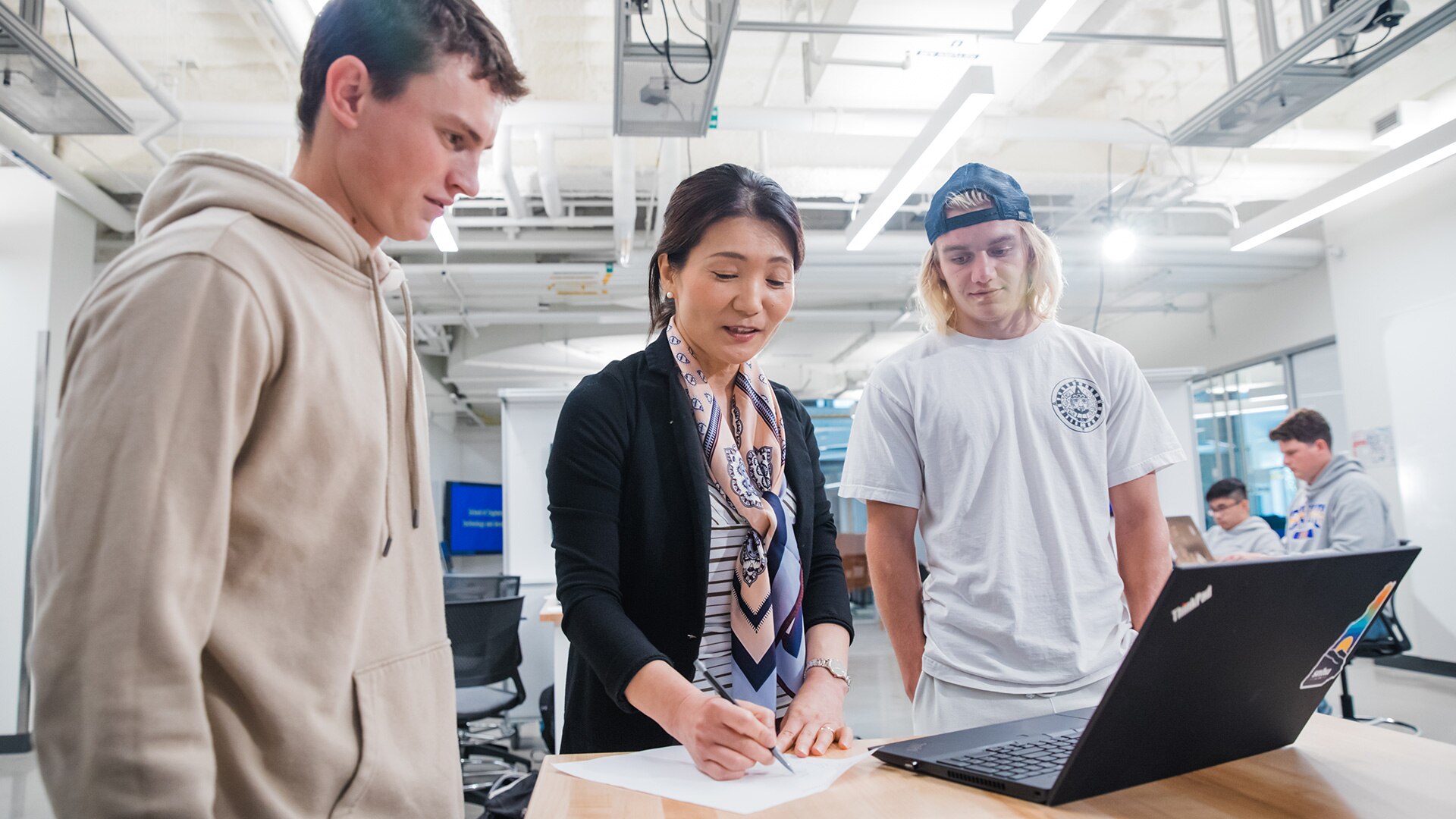 Two students with a laptop, in discussion with their professor.
