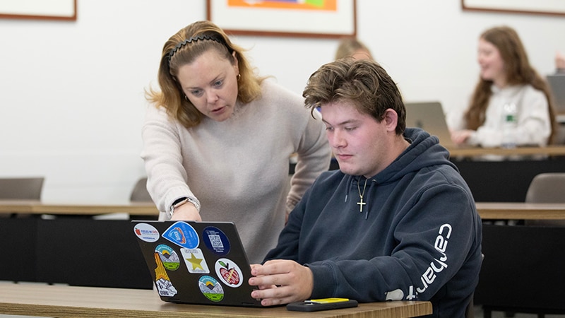 An instructor pointing at a student's laptop while they both look at the laptop screen.