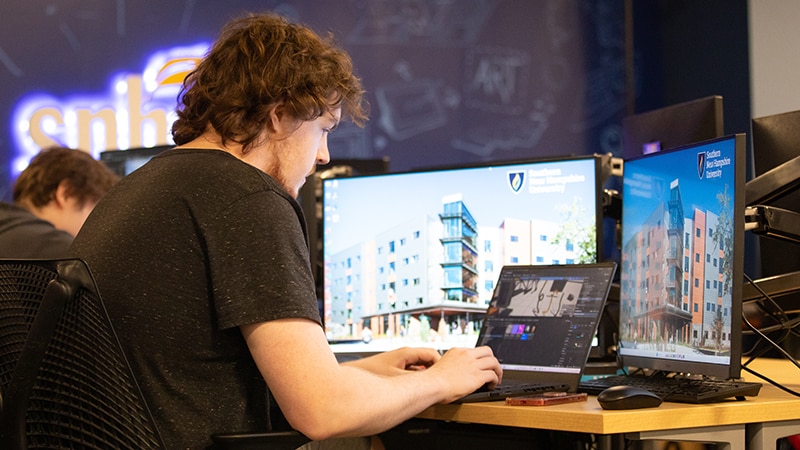 Student working on laptop and desktop computers in classroom setting.