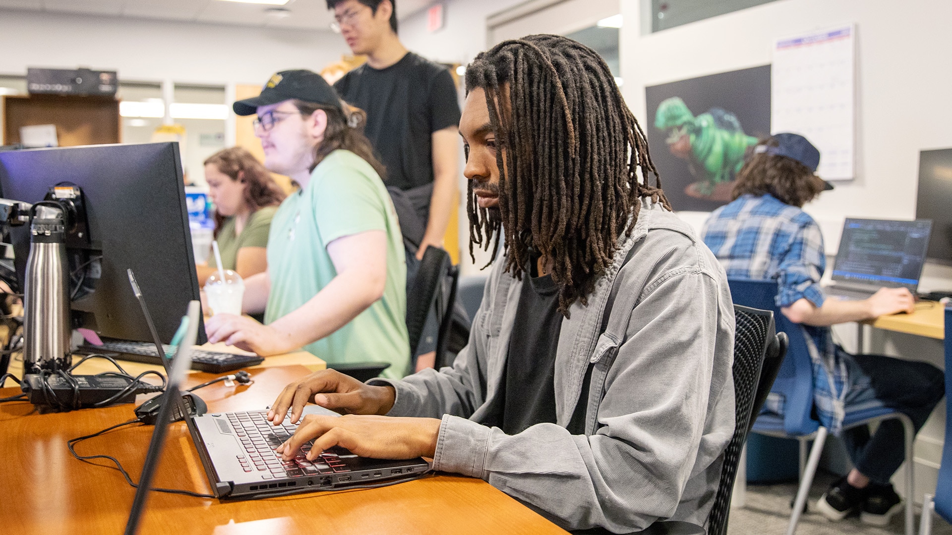 A student typing on a laptop and other students in the classroom working on their computers.