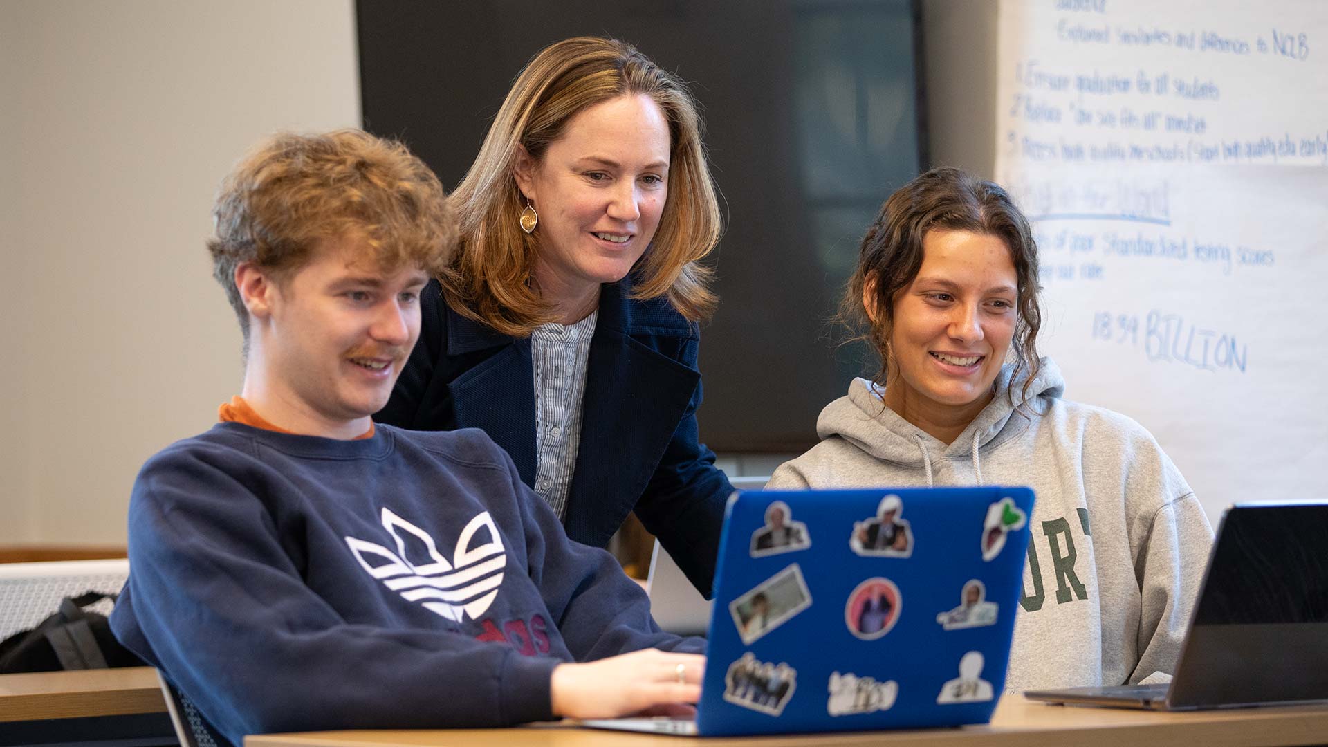 A Professor in discussion with two of her students with their laptops in the classroom.