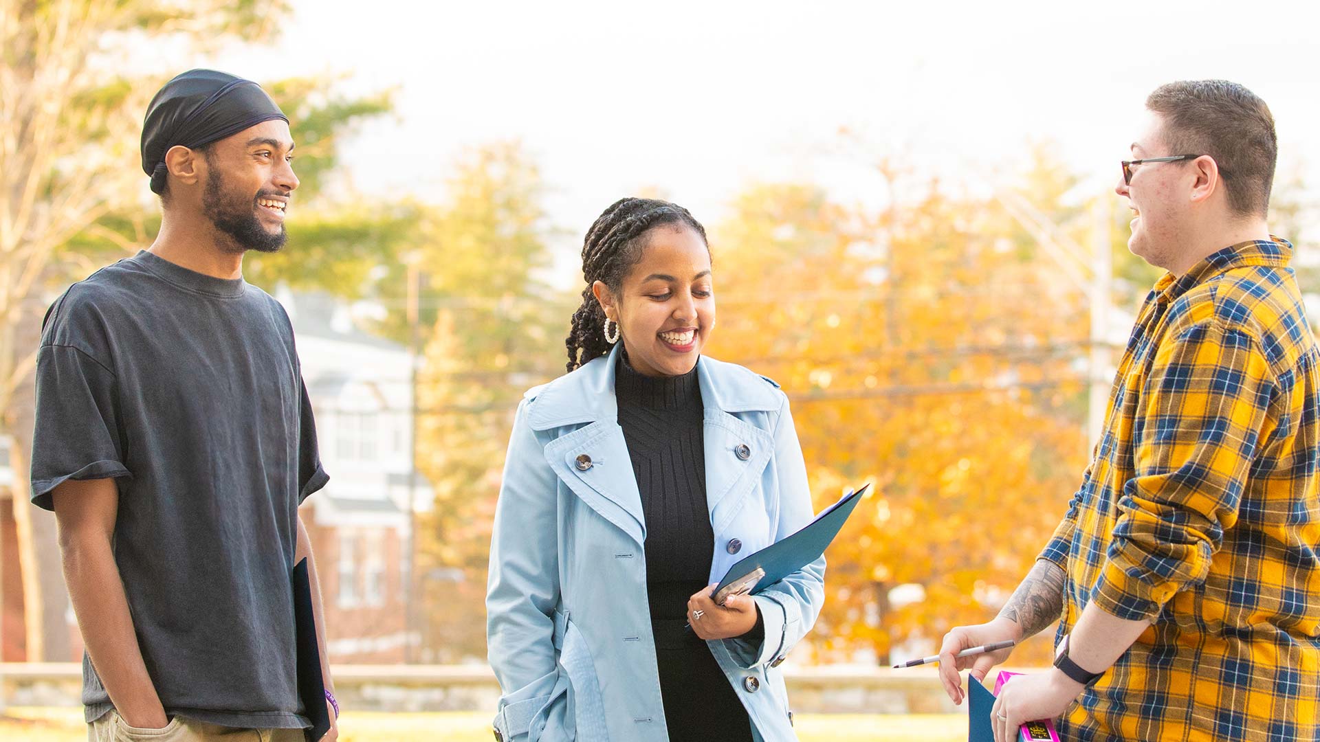 Three people standing outdoors on a sunny day, smiling and chatting.