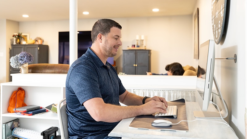 Person typing at a desk with a computer in a cozy, well‑lit living room workspace.
