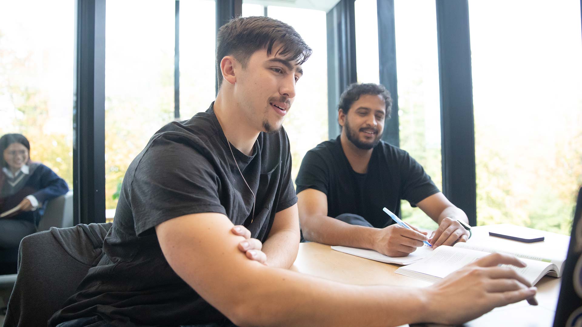 Two individuals sitting at a table discussing a book and taking notes.