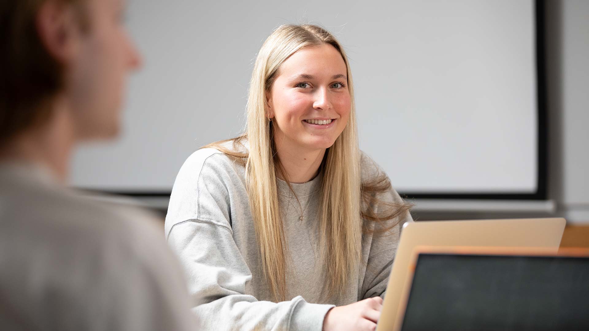 A student sitting and smiling, with a laptop in front of them.