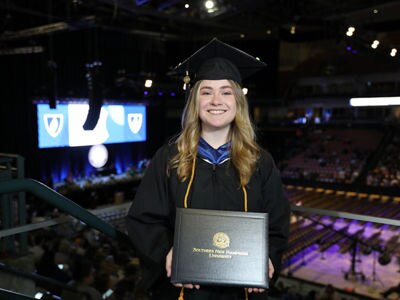 Kayleigh Maier, who earned her bachelor's in English and creative writing from SNHU in 2023, wearing her graduation cap and gown and holding her diploma.