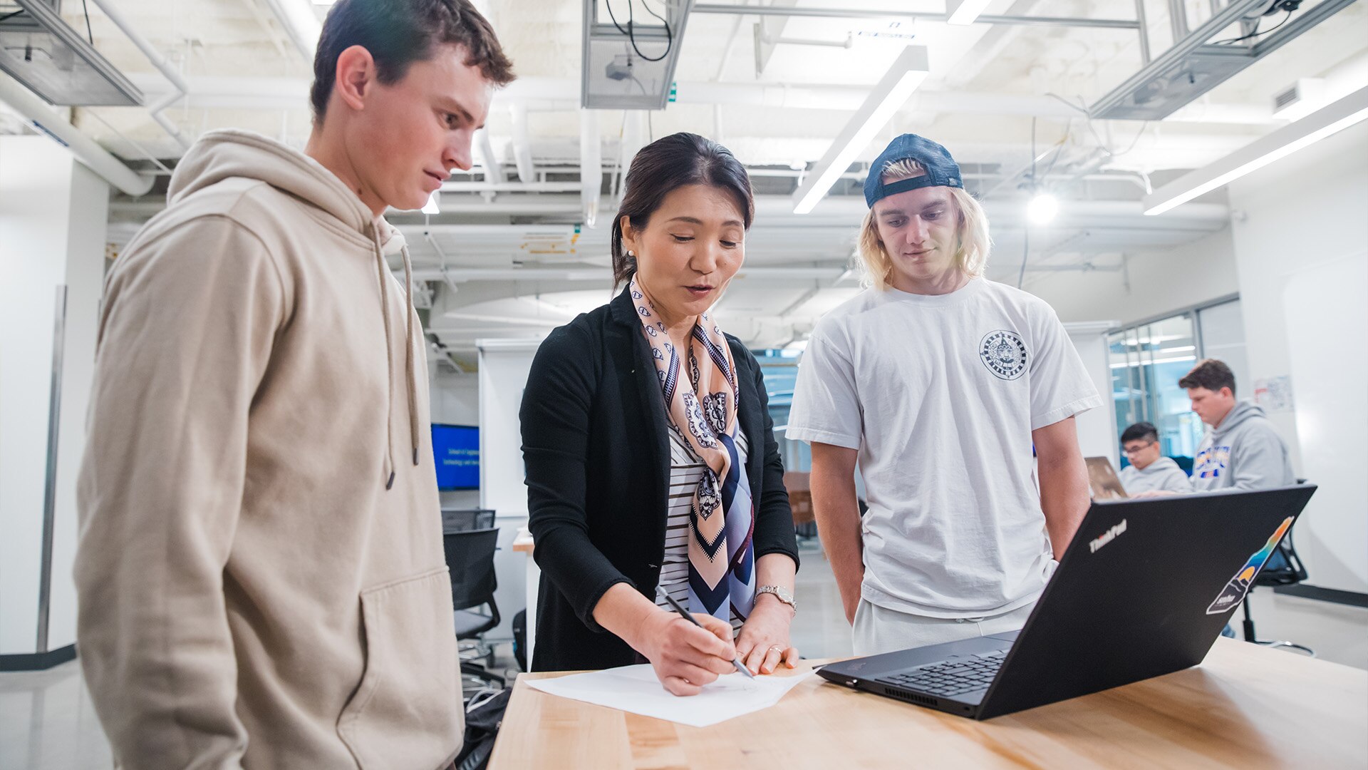 Two students with a laptop, discussing an assignment with the professor