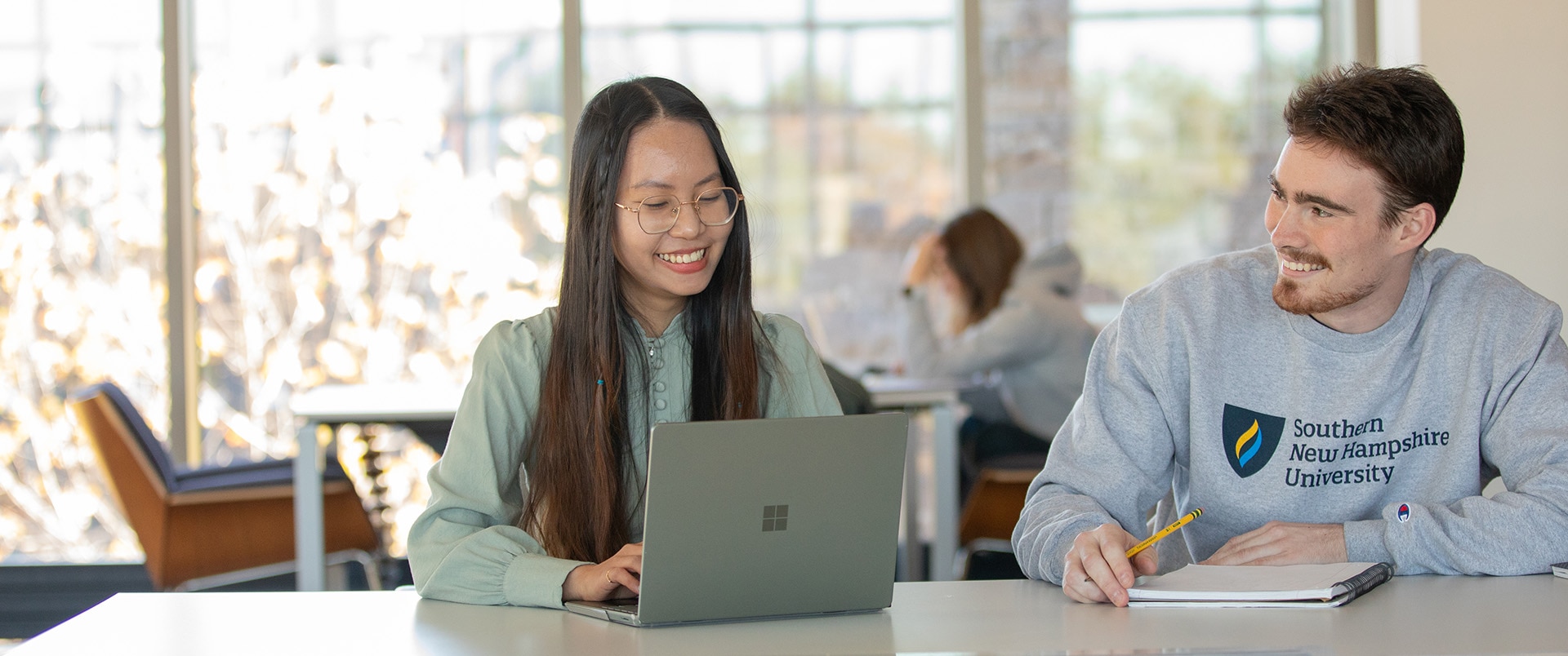 Alice Nguyen, left, works on her laptop while engaging with fellow SNHU business student, Spencer Deane, who writes in his notepad.