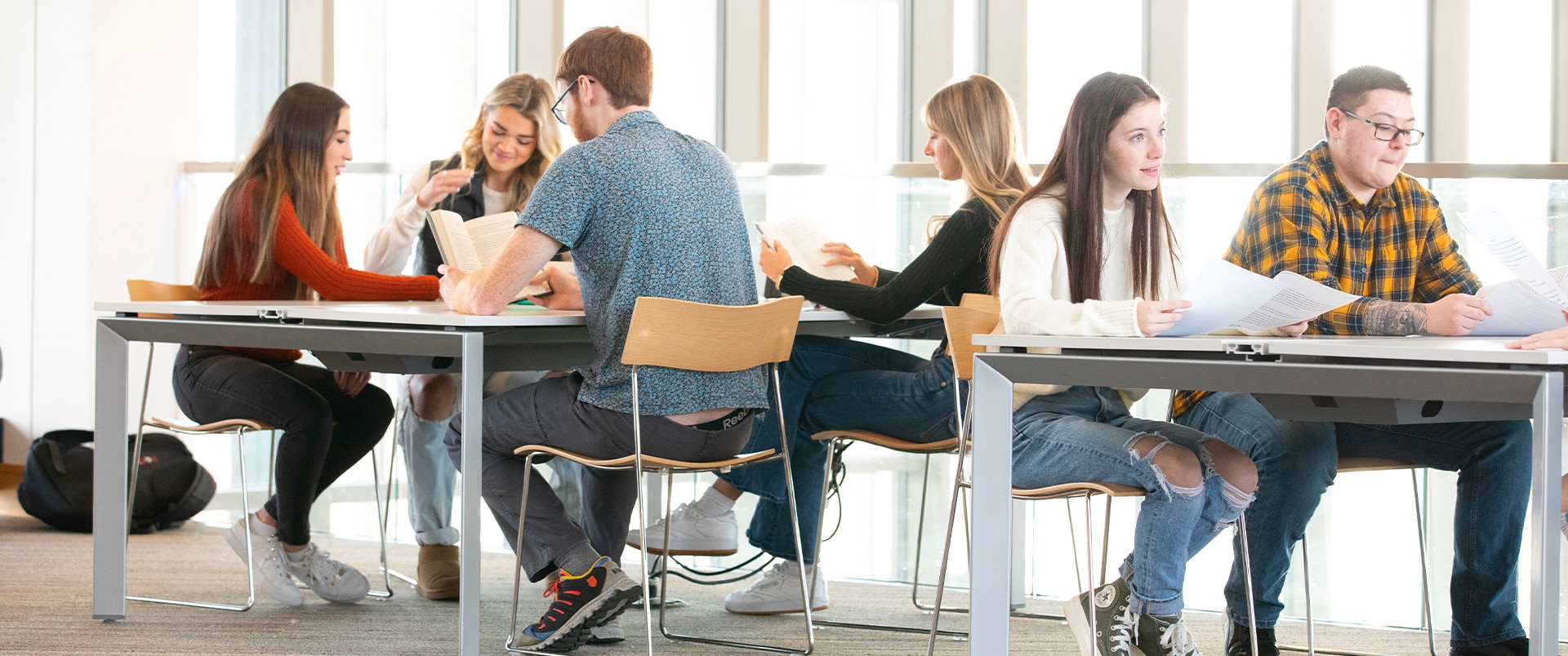 Two groups of students sitting together at a table, discussing and reviewing notes in a study space.