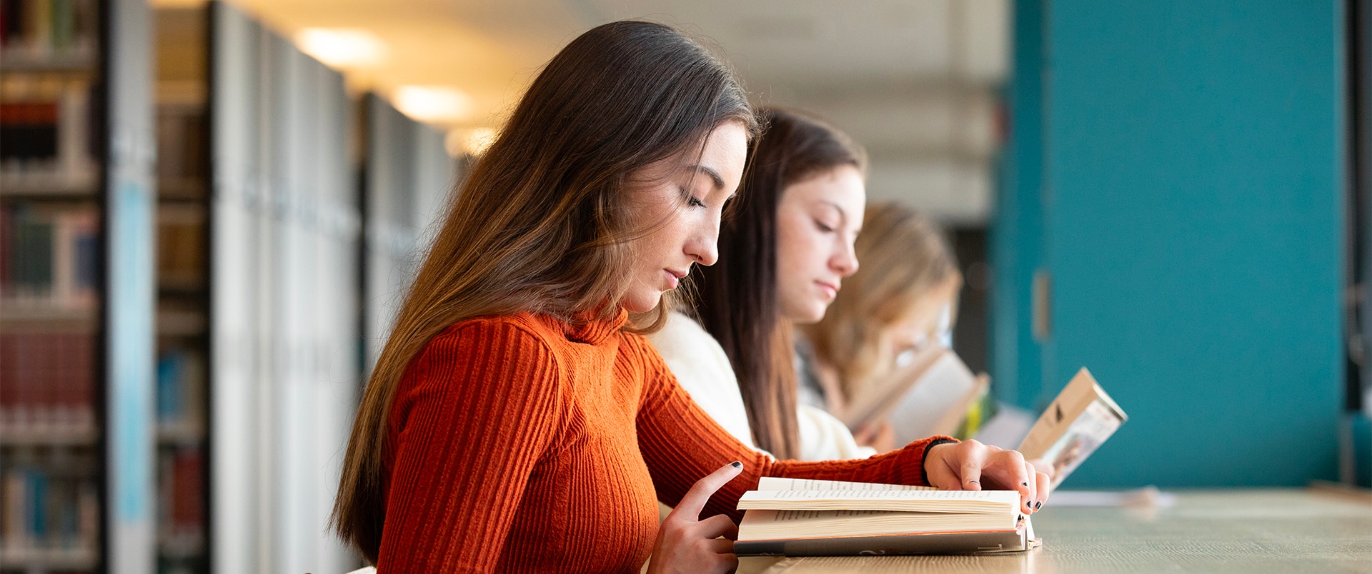 Three girls sitting and reading books in a library.