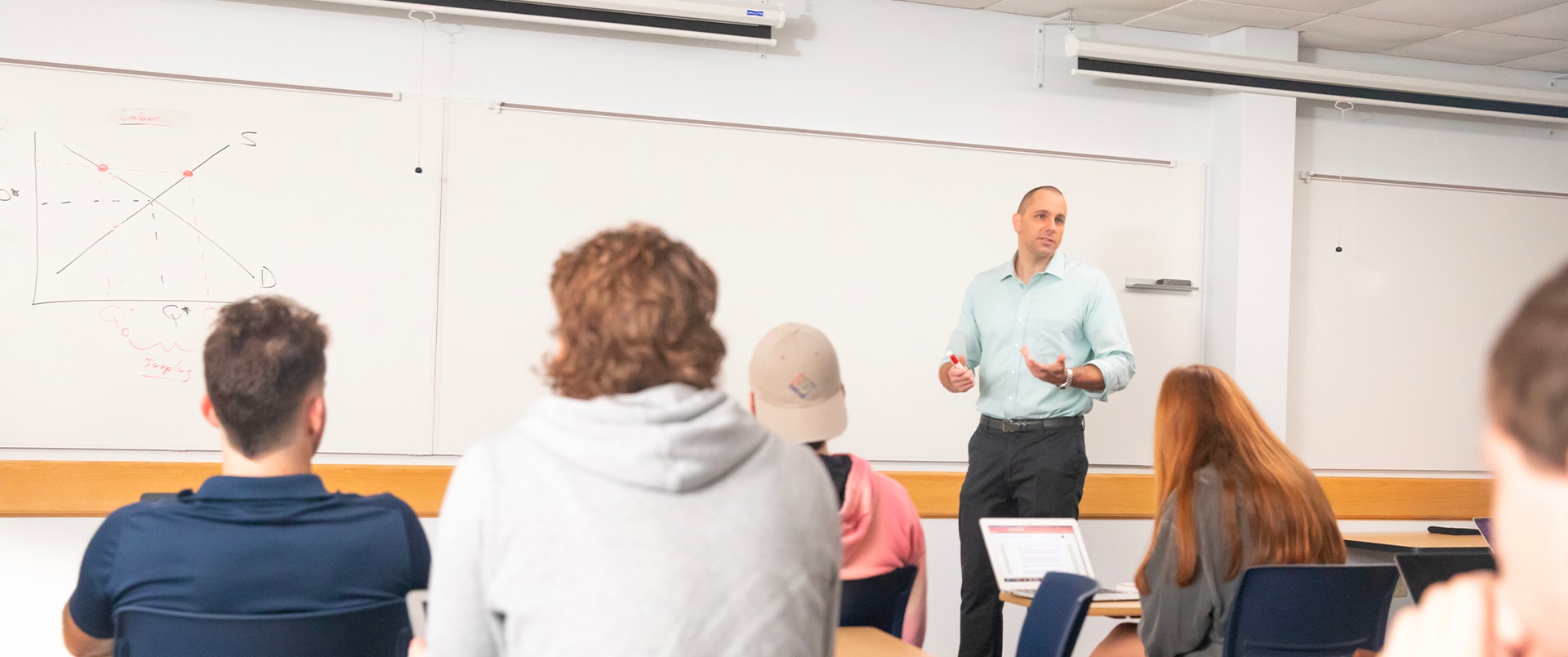 An instructor discussing a mathematical problem with a group of students in a classroom.