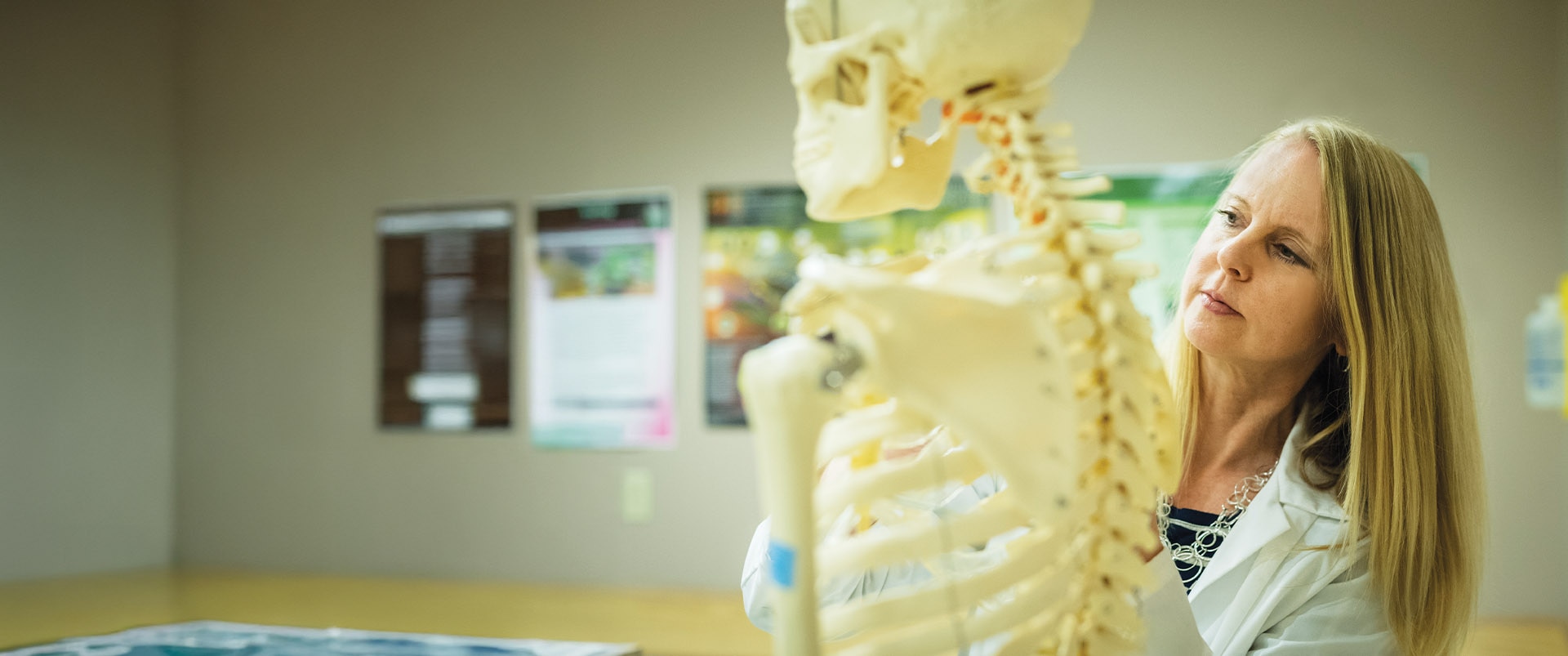 An instructor in a classroom setting observing and moving a model skeleton.