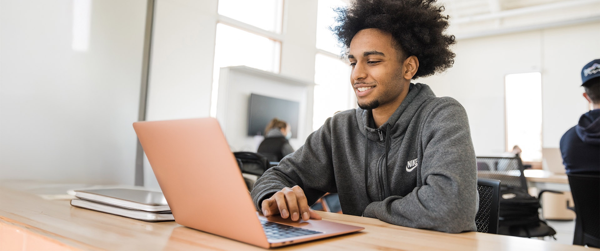 A student sitting in a classroom while using a laptop.
