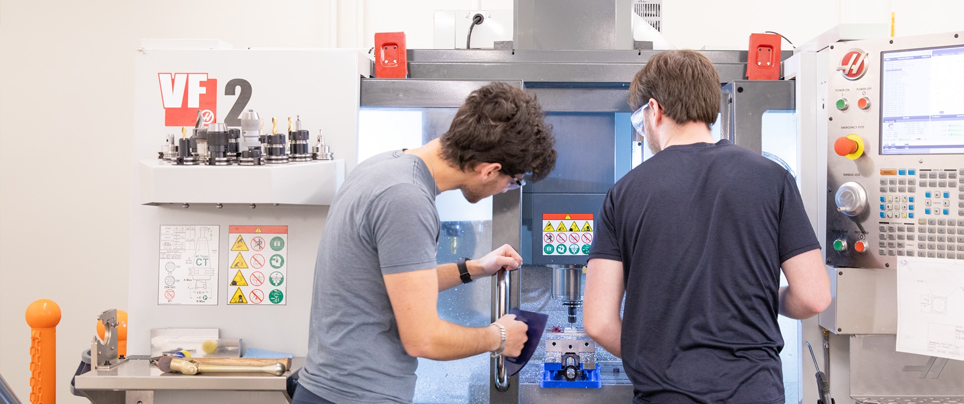 Two individuals work together on a computer numerical control machine in a lab.