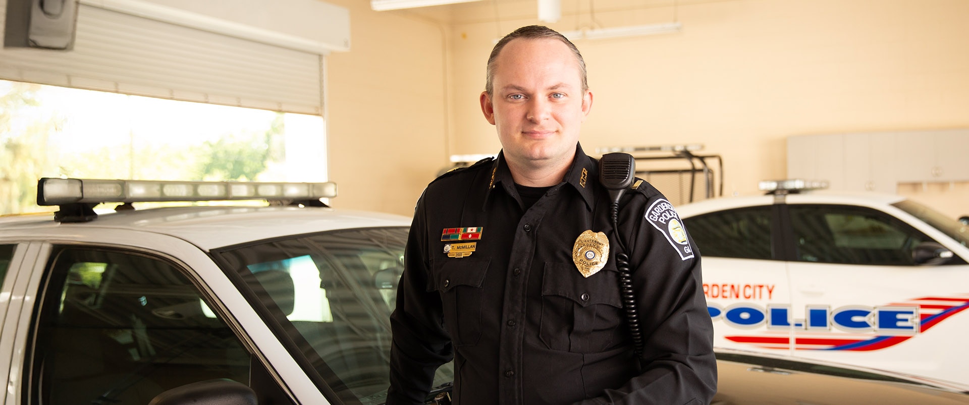 A law enforcement official standing inside a garage near two police vehicles.