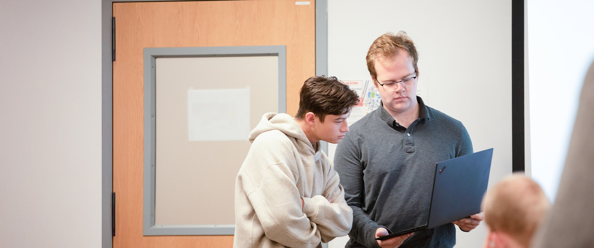 Two students presenting in front of a classroom and looking at a laptop.