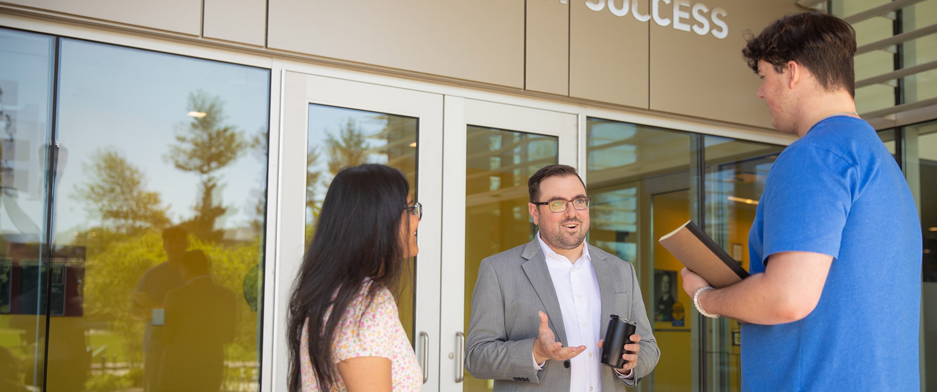 Students in conversation with their professor, outside the college building.