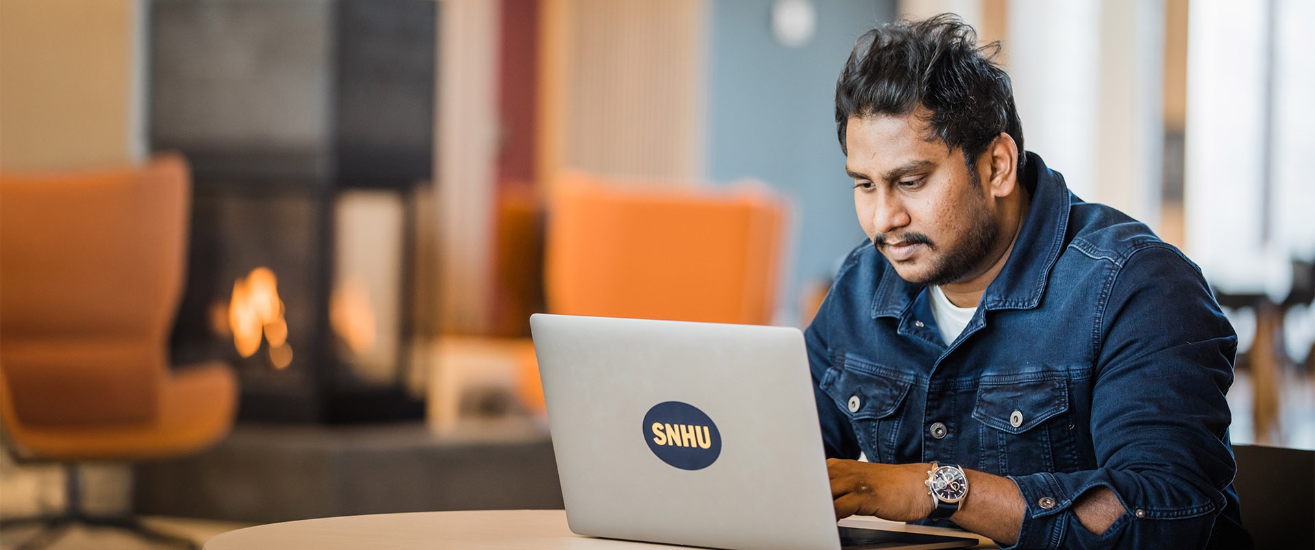 A student sitting in a study area while typing on his laptop.