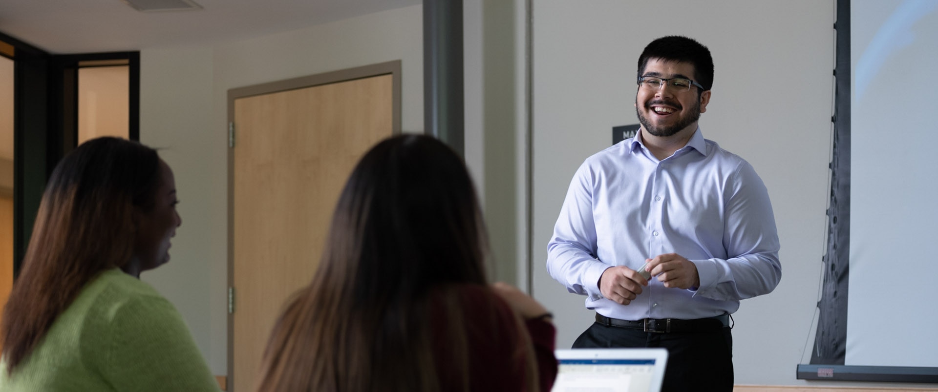 An instructor standing in front of a classroom and smiling.