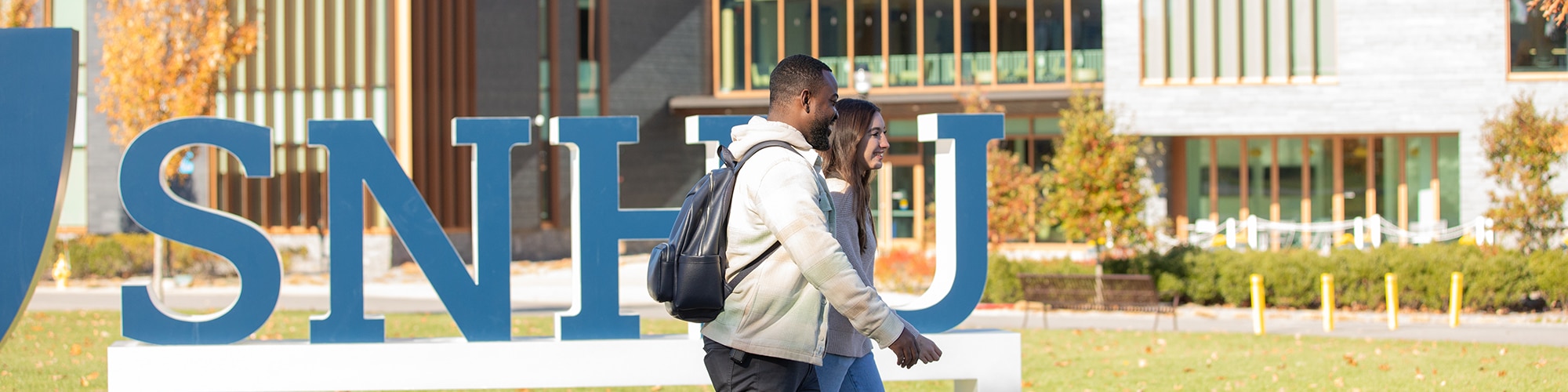 Two students walking on the SNHU campus with an SNHU logo sign in the background.