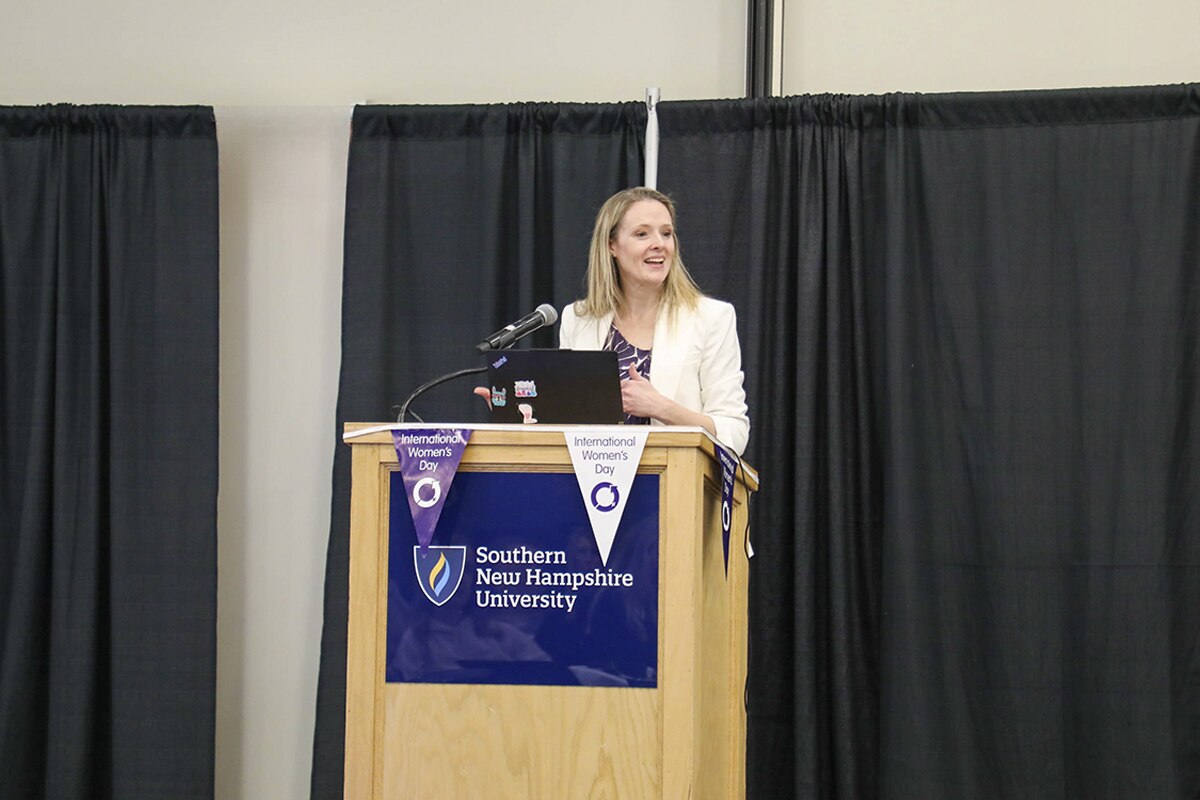 Dr. Sarah Buhrlage, standing behind podium, speaking at SNHU campus for International Women's Day.