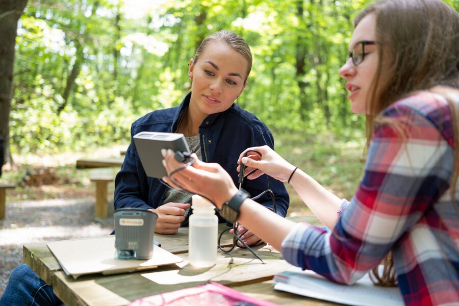 Two students discussing a project and looking at a field instrument in an outdoor classroom.