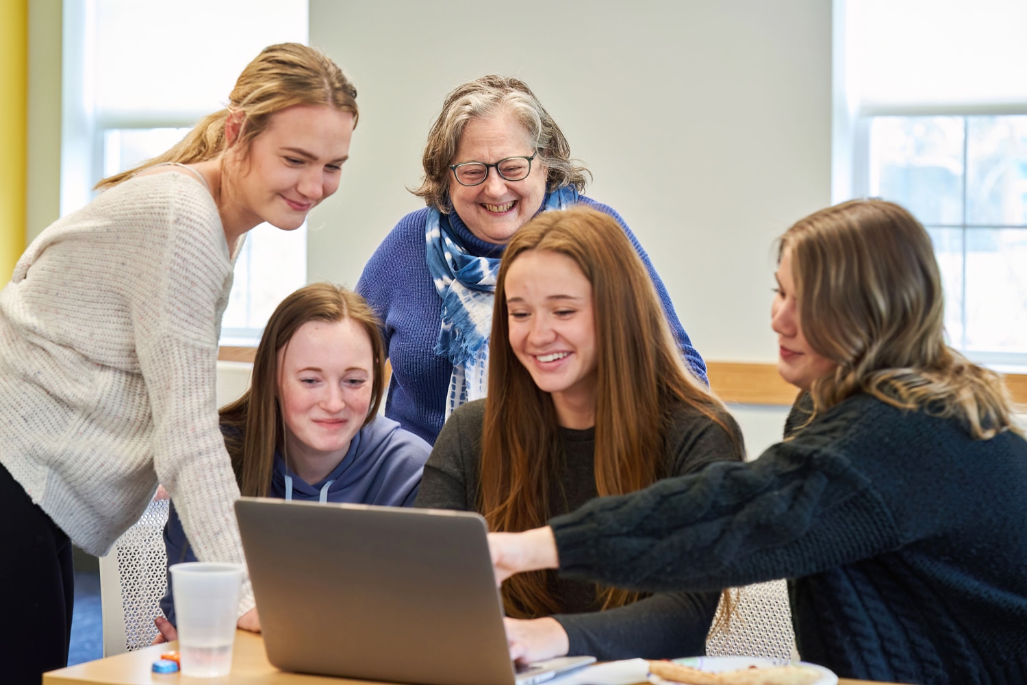 A group of students and a professor collaborating on a project on a laptop.